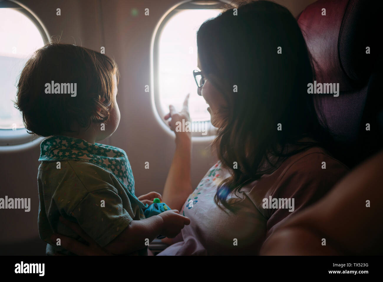 Mother and little daughter on airplane looking out through the window Stock Photo