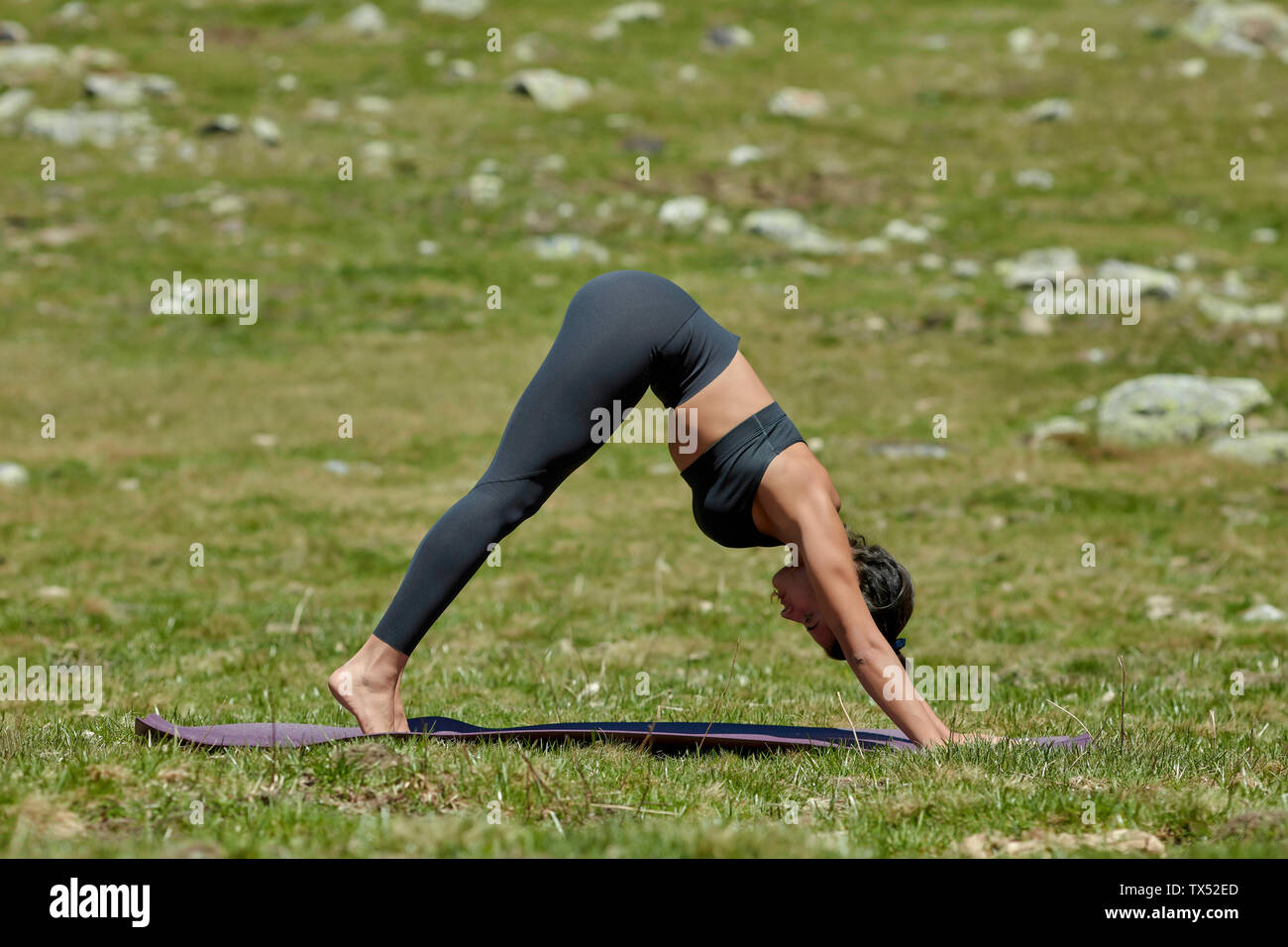 Young woman doing yoga on meadow, downward facing dog position Stock Photo