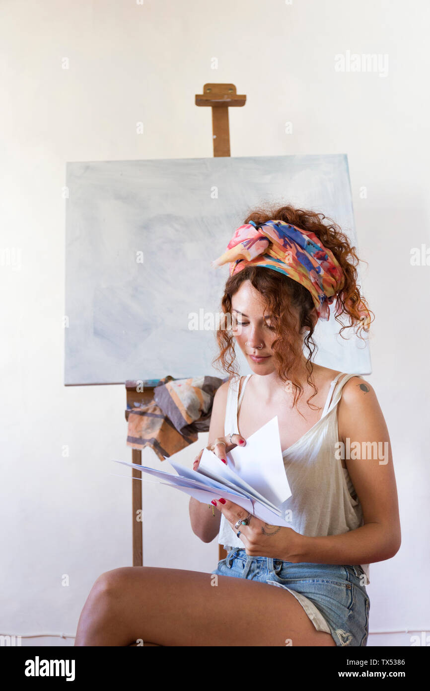 Young female painter in art studio next to empty canvas looking at papers Stock Photo