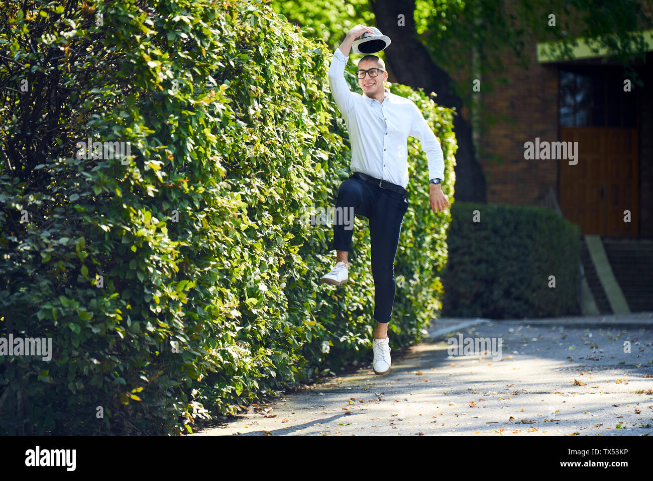 Happy young man jumping around at a hedge Stock Photo
