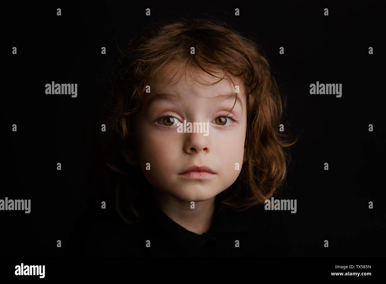 5 year old boy with long hair studio portrait on black background Stock Photo