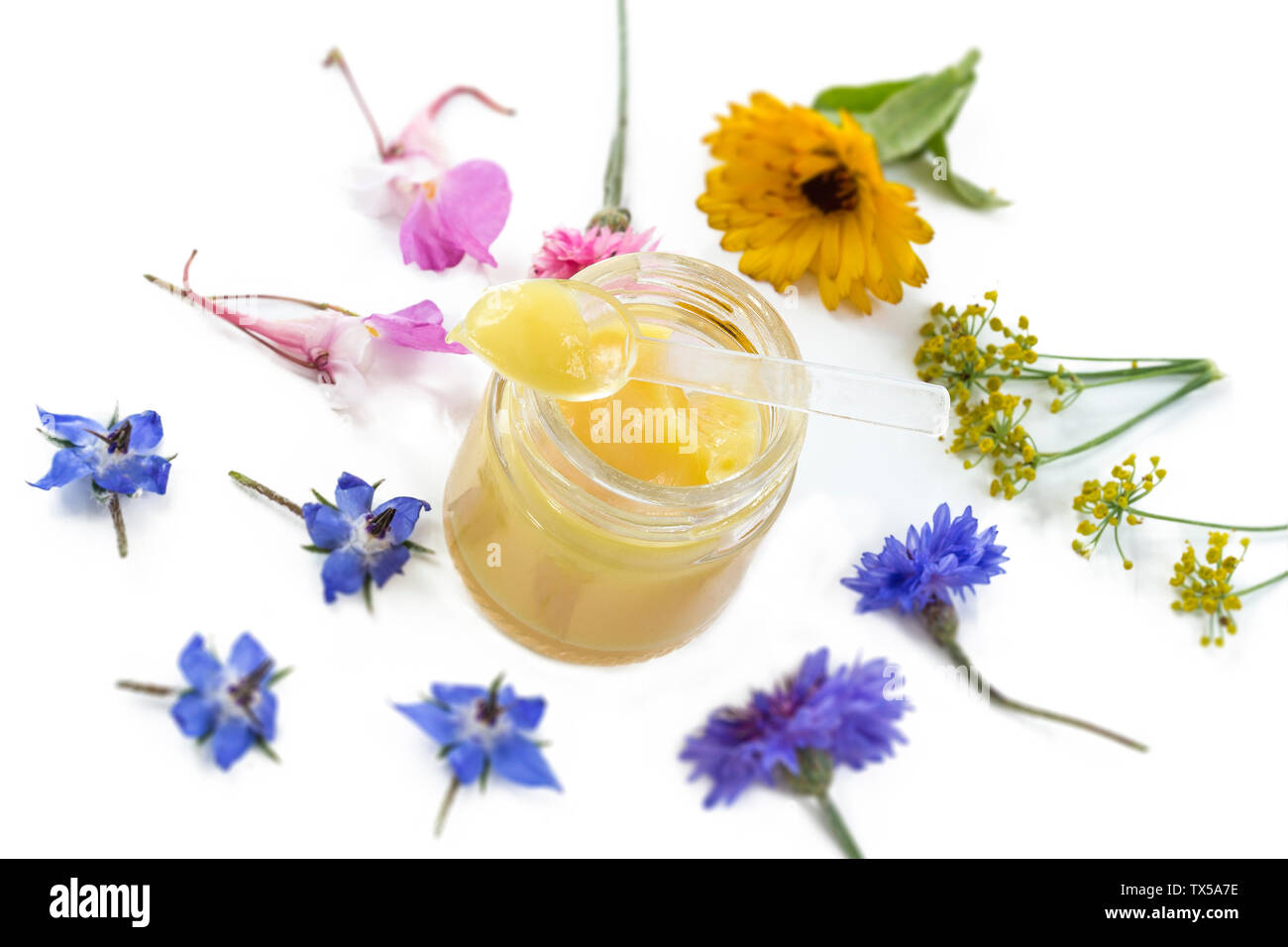 Raw organic royal jelly in a small bottle with litte spoon on small bottle surrounded by flowers on old white background. Stock Photo