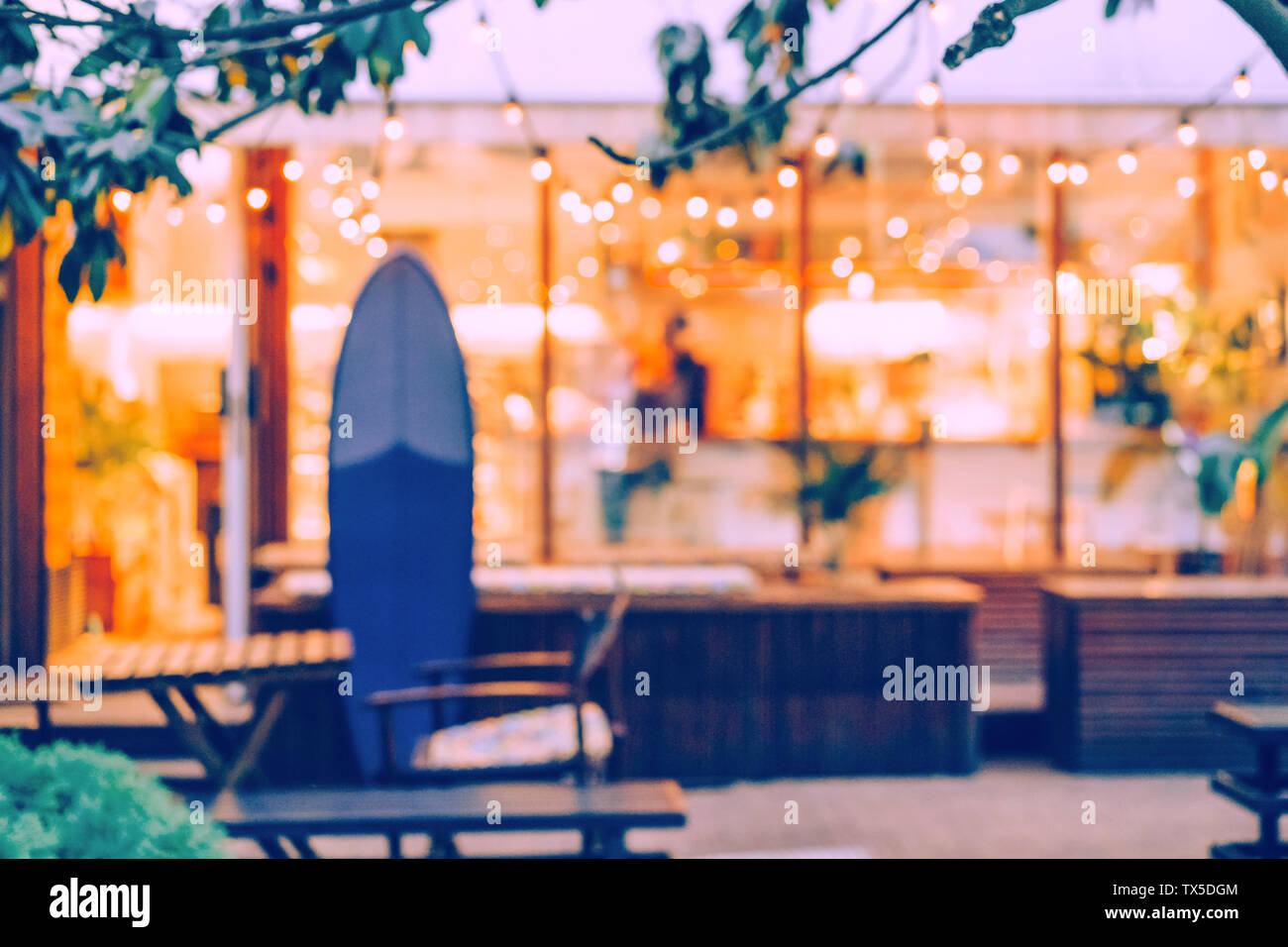 The defocused background of the summer coffee house, in the foreground a surfboard, a garland with light bulbs creates a cosiness in the interior, a m Stock Photo