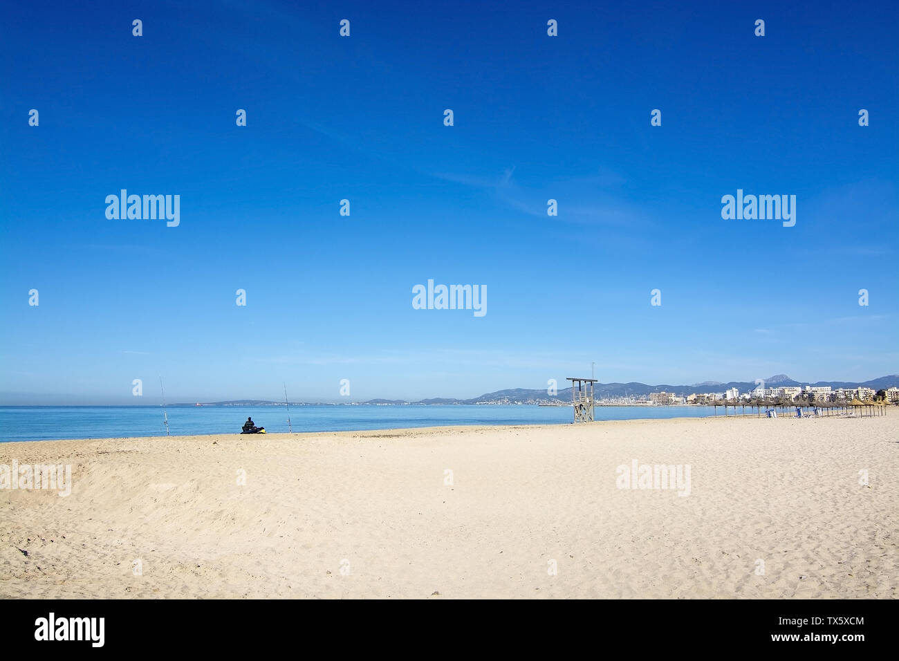PALMA, MALLORCA, SPAIN - MAY 1, 2019: Man fishing from a sandy beach with life guard tower and blue sky on May 1, 2019 in Palma, Mallorca, Spain. Stock Photo