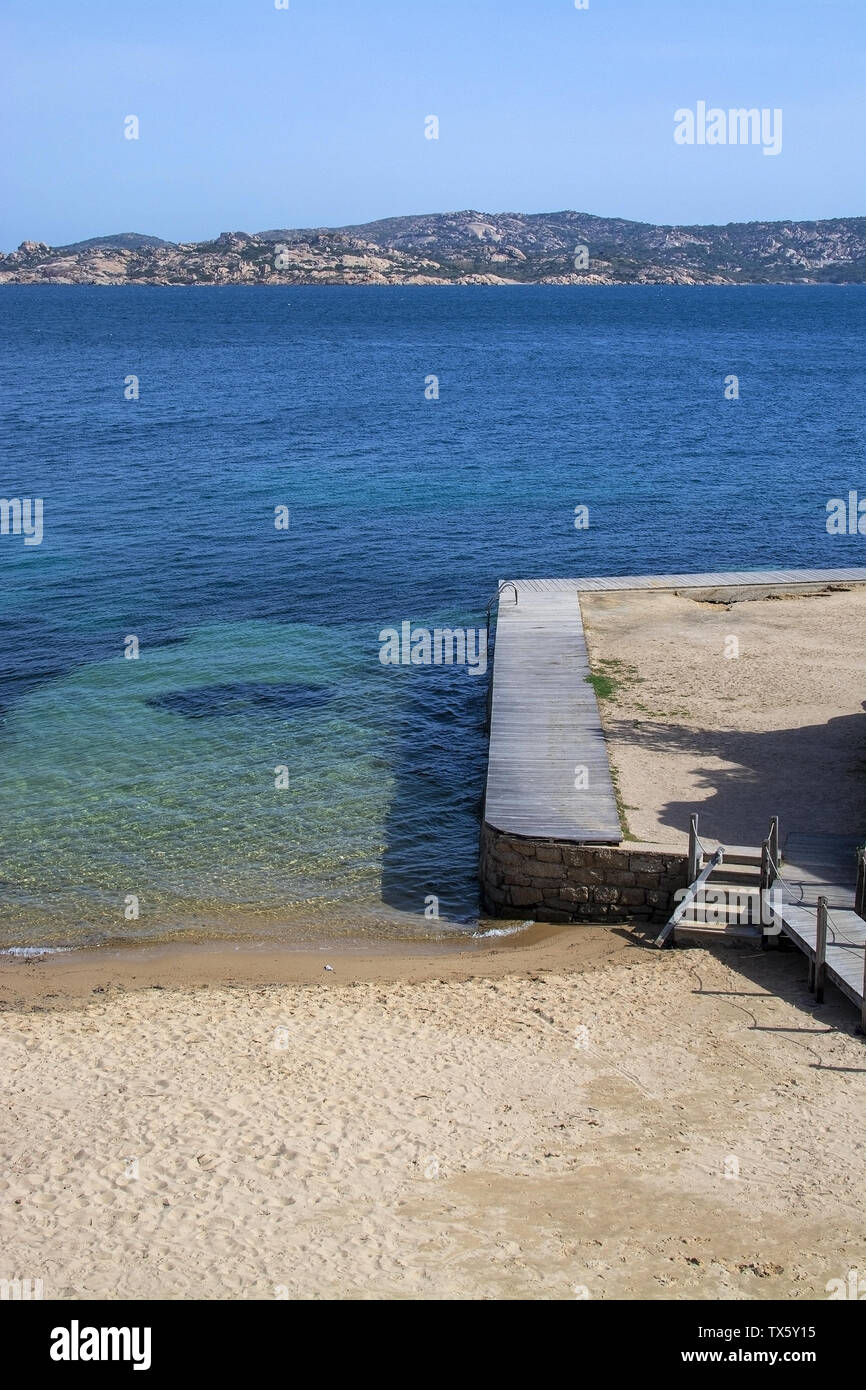 Sandy beach and wooden boardwalk near green water in Costa Smeralda, Sardinia, Italy. Stock Photo