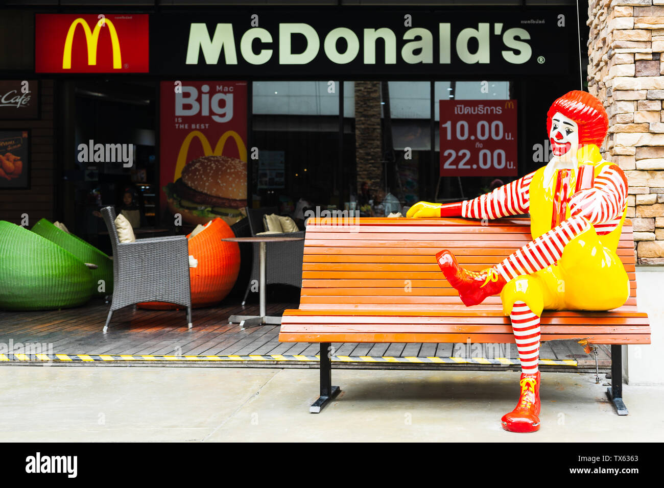 BANGKOK, THAILAND - 2019 JUNE 16: Ronald McDonald character sitting on bench, in front of McDonalds restaurant. Ronald McDonald is a clown character u Stock Photo