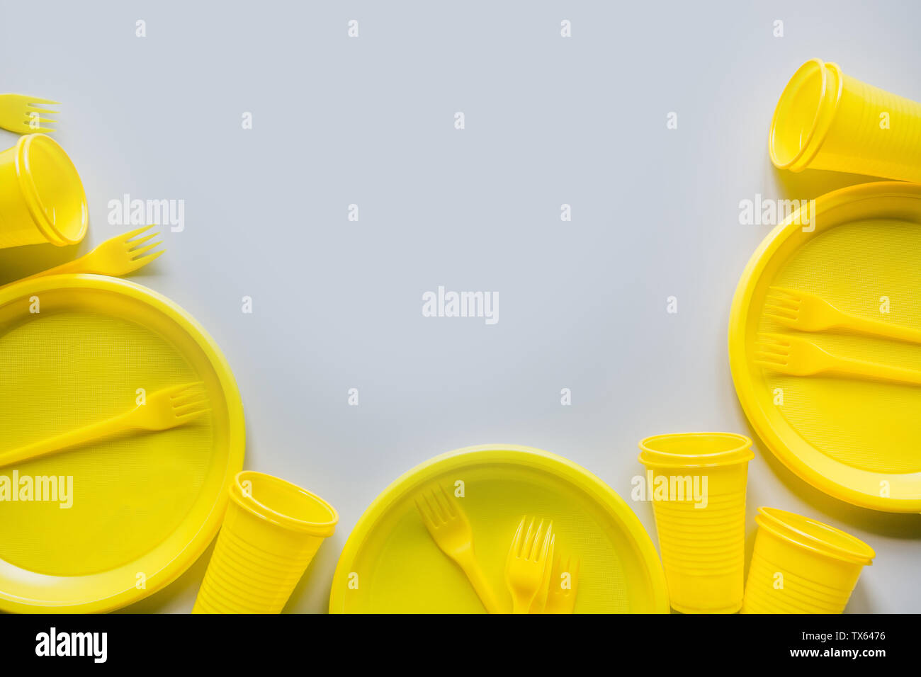 Single use picnic yellow utensils, plates, cups, forks on grey