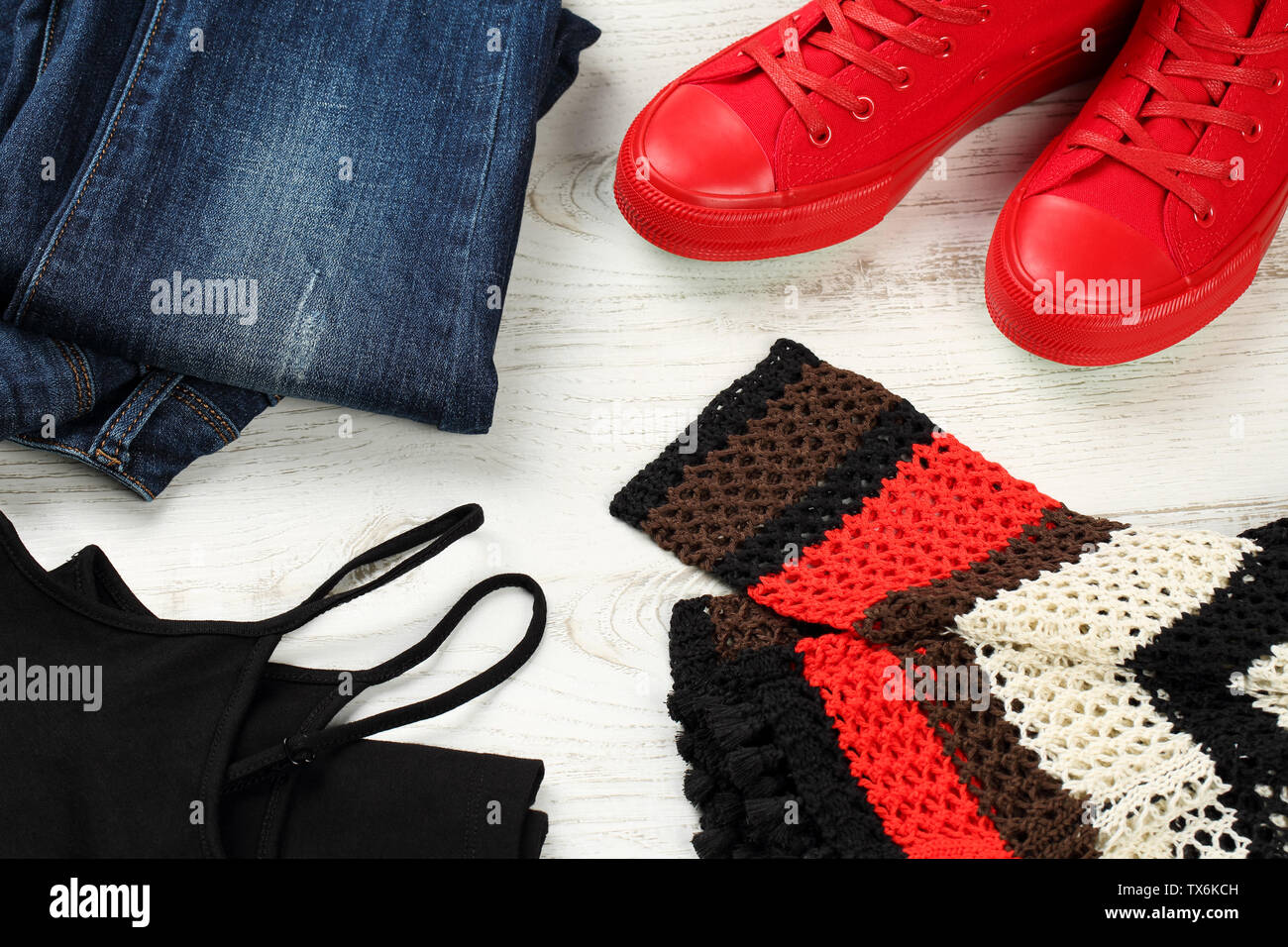 Close up, flat lay of casual clothing details for women - blue jeans, red sneakers, black sleeveless tank top and multicolored, hand knitted cotton bl Stock Photo