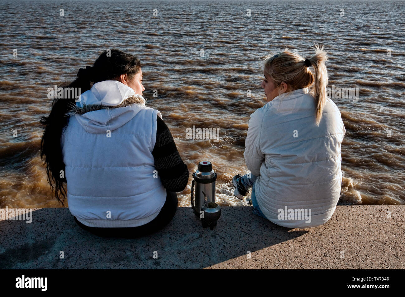 Two girlfriends chatting along la Plata river in Montevideo Uruguay Stock Photo