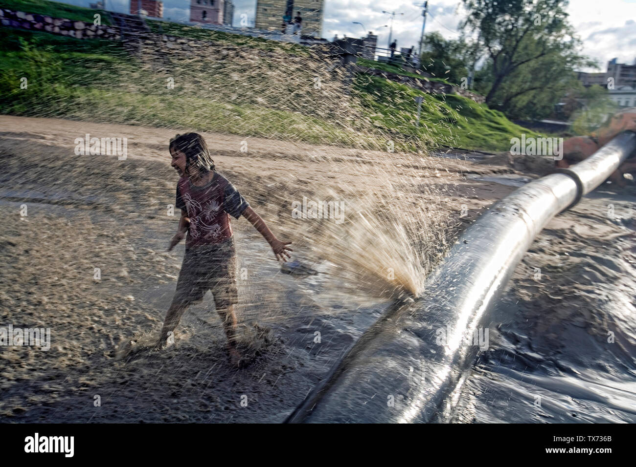 A child is playing with a broken water pipe used to pull water from the Paraguay river overflow after the heavy rain fall, Asuncion, Paraguay Stock Photo