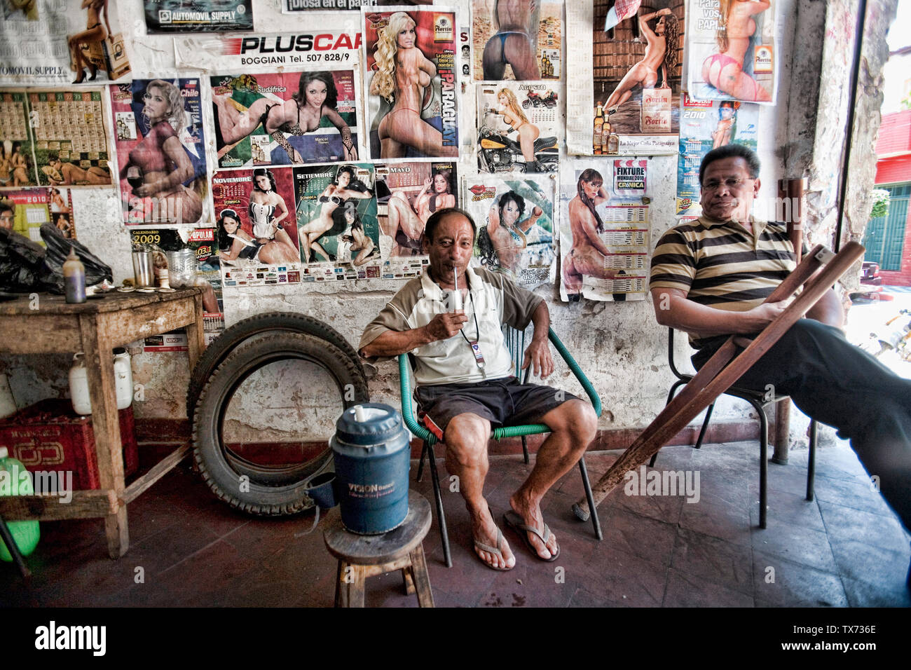 Two men relaxing and drinking mate in a motorbike workshop in la Chacarita shanty town, Asuncion, Paraguay Stock Photo
