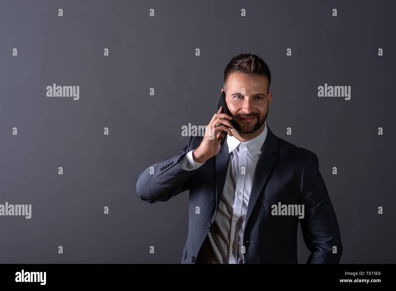 A smiling handsome young businessman in a suit talking on his phone in ...
