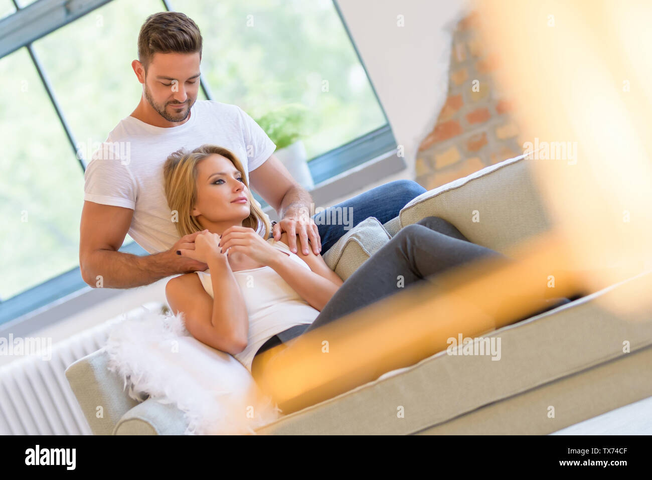 A beautiful young woman lying on the sofa with boyfriend hugging her ...
