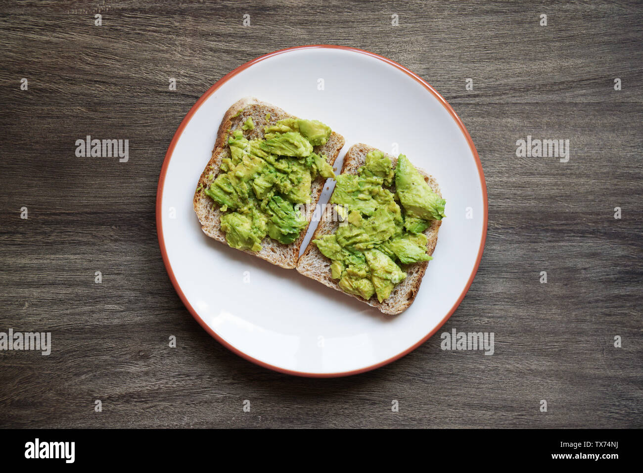 top view of two slices of homemade avocado toast on a plate on rustic wooden table - hipster food trend Stock Photo