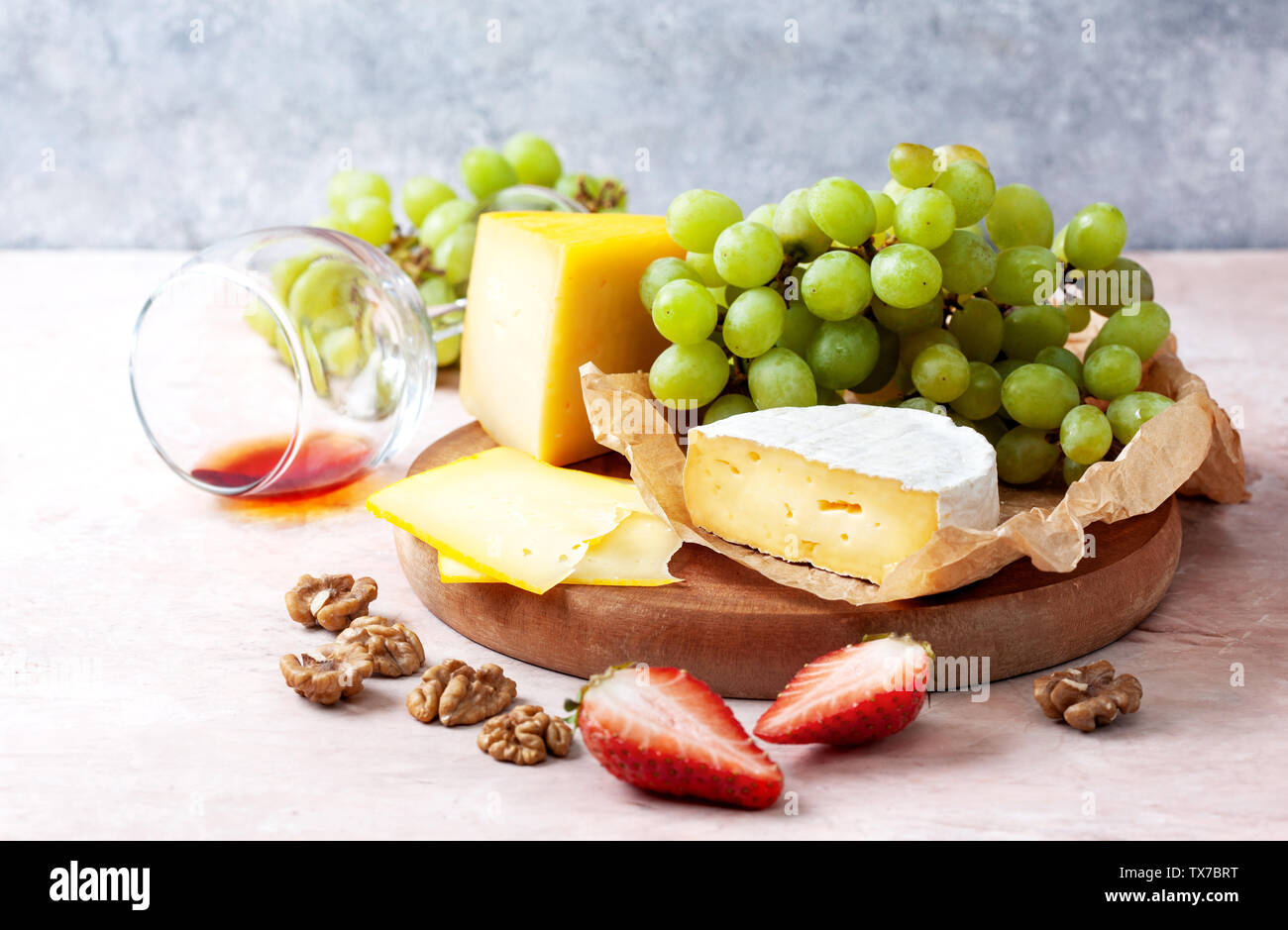 different cheeses with strawberries and grapes on a wooden board closeup Stock Photo