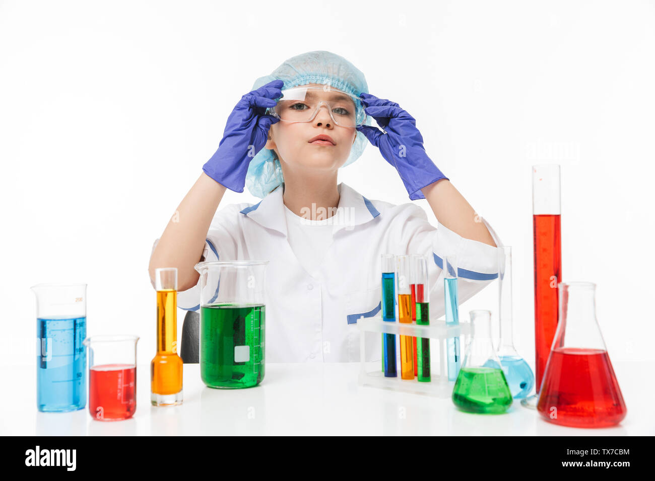 Portrait of serious little girl in white laboratory coat making chemical experiments with multicolored liquid in test tubes isolated over white backgr Stock Photo