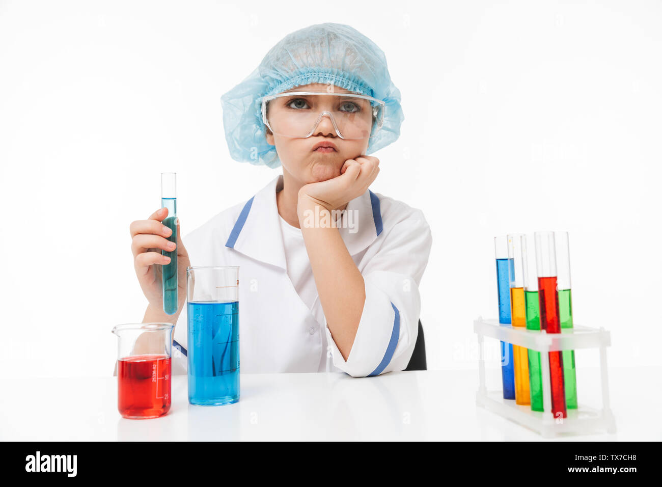 Portrait of focused little girl in white laboratory coat making chemical experiments with multicolored liquid in test tubes isolated over white backgr Stock Photo