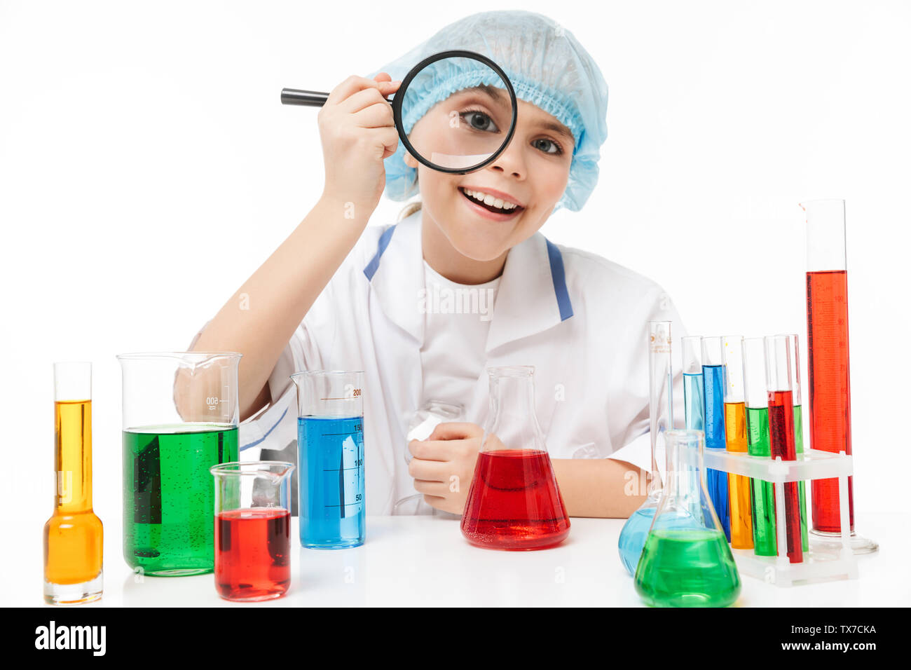 Portrait of microbiologist little girl in white laboratory coat holding magnifying glass during chemical experiments isolated over white background Stock Photo