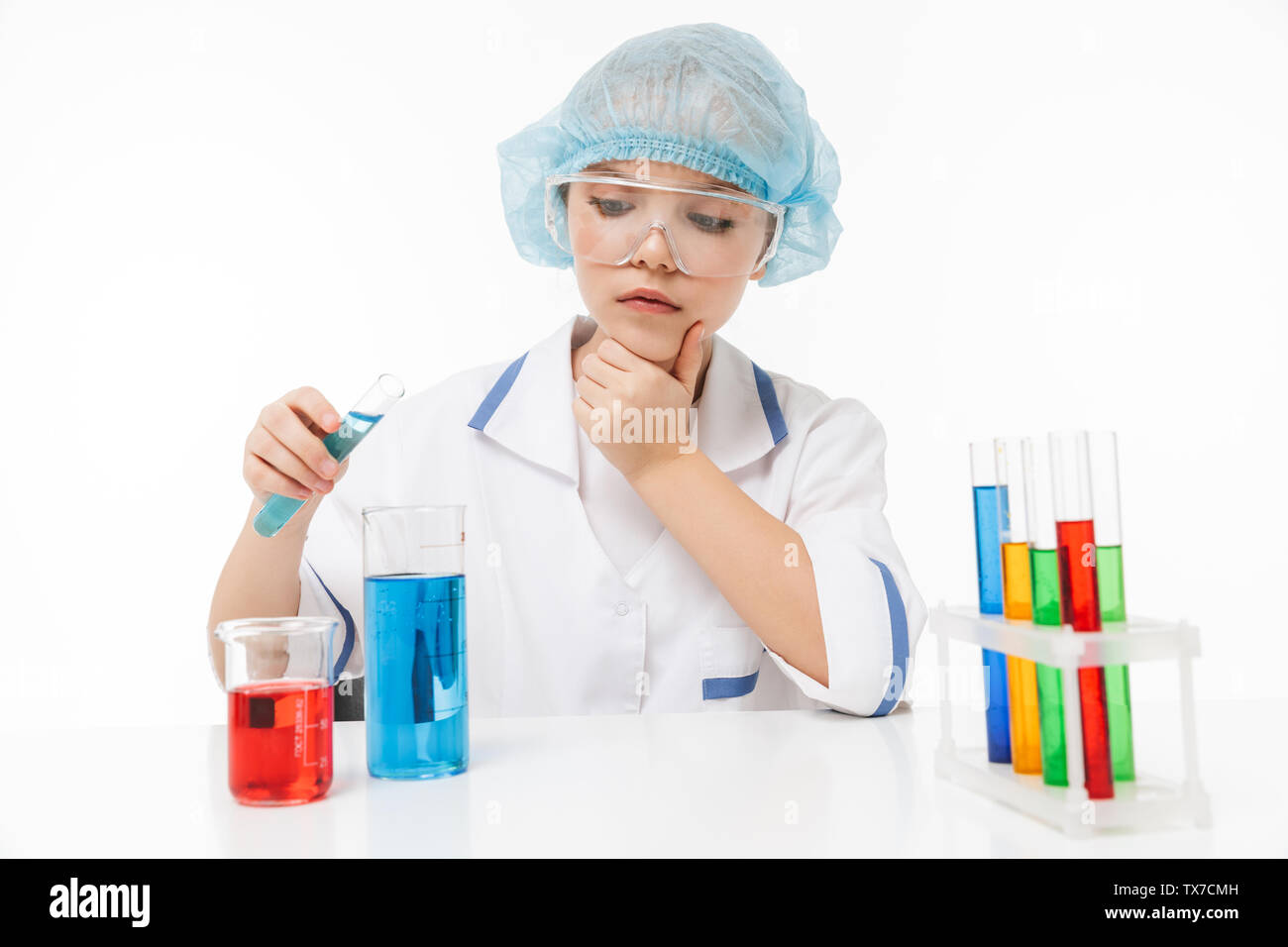 Portrait of concentrated little girl in white laboratory coat making chemical experiments with multicolored liquid in test tubes isolated over white b Stock Photo