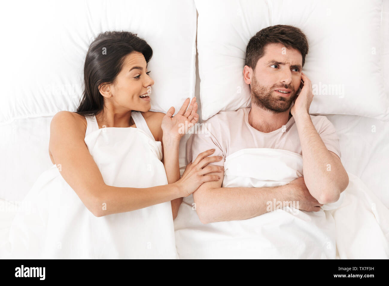Image of a happy woman talking to her confused young man in bed under ...