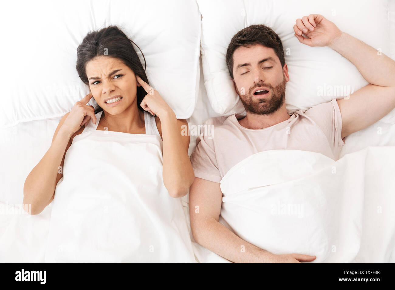 Image of a displeased woman covering ears near her man sleeping in bed