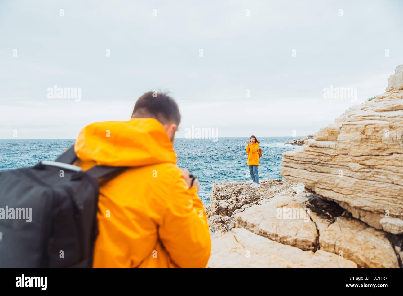 man taking picture of woman in yellow raincoat at the cliff near ...