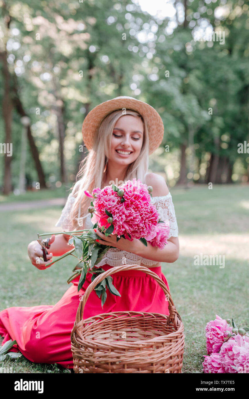 Romantic woman florist in straw hat makes a bouquet with pink peonies ...
