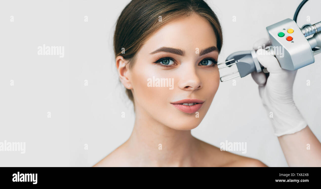 woman with perfect clear skin getting laser facial treatment, aesthetic face surgery on light background Stock Photo