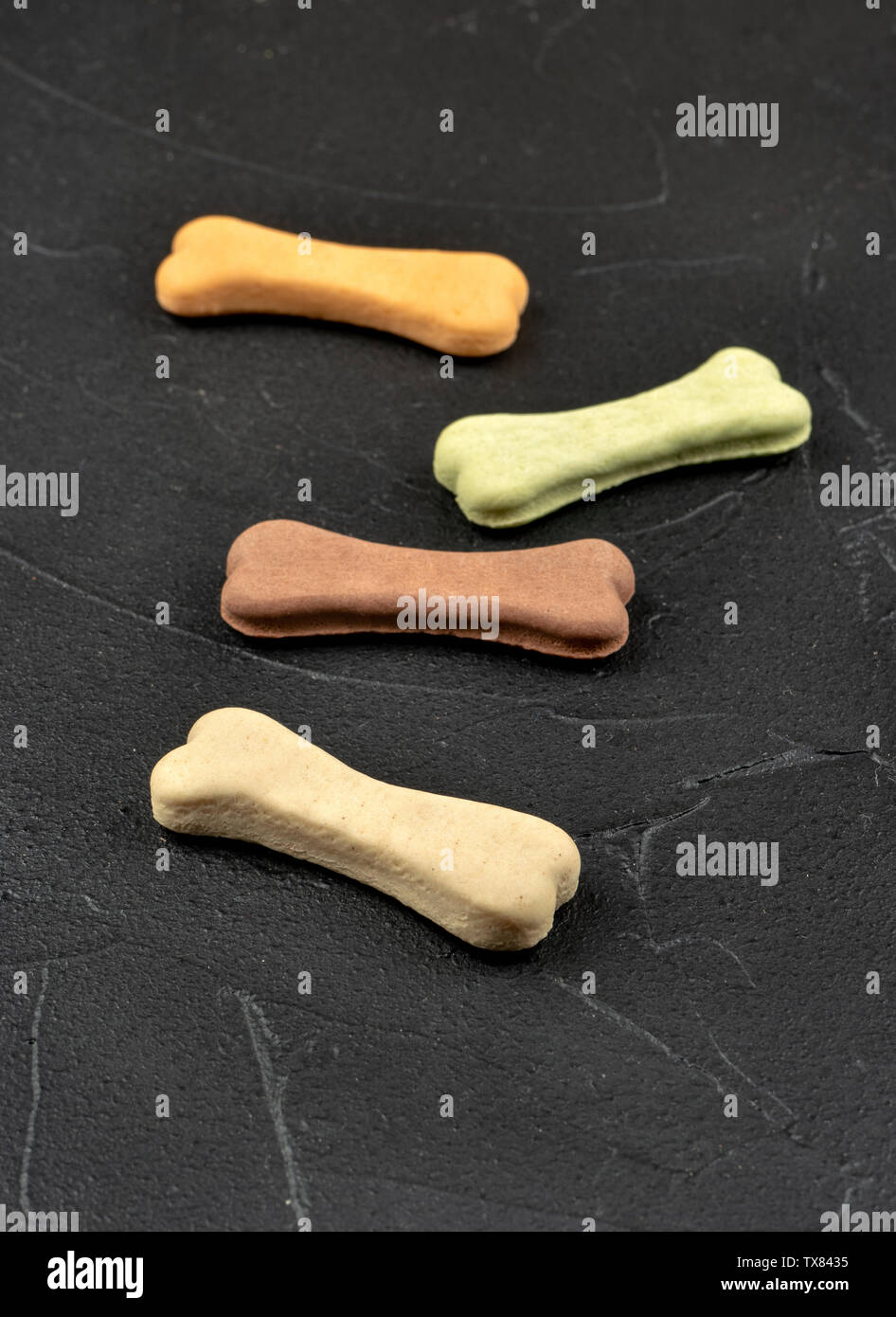 Four bone-shaped dog biscuits on a dark background Stock Photo
