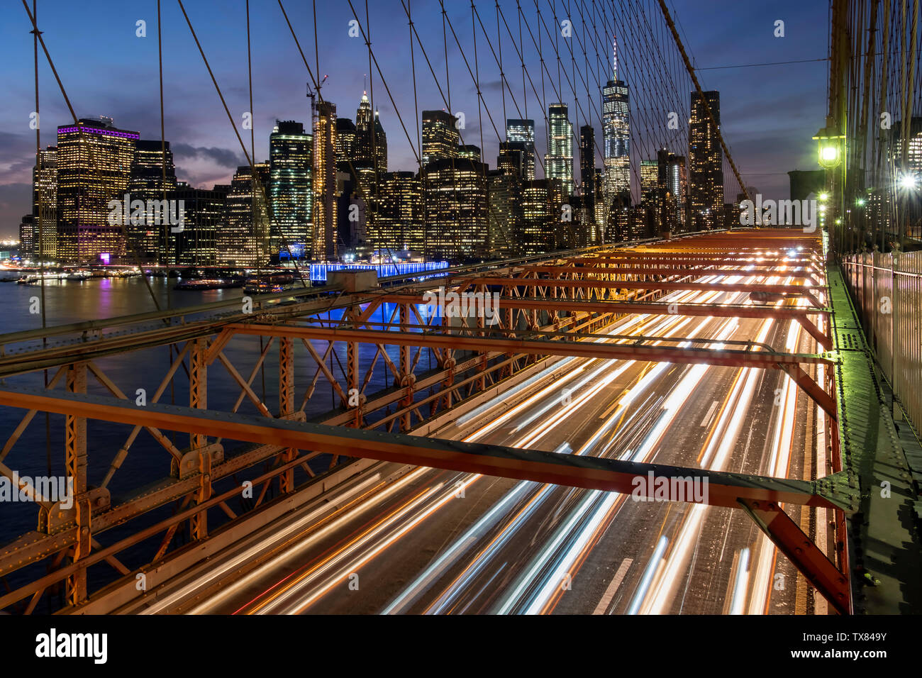 Traffic crossing the Brooklyn Bridge backed by the Manhattan skyline at night, New York, USA Stock Photo