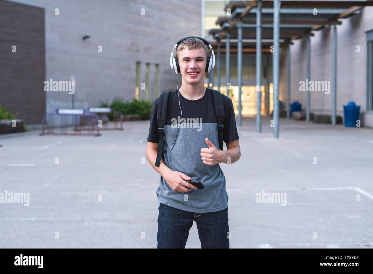 Excited teenager listening to music with his headphones while standing outside of school. Stock Photo