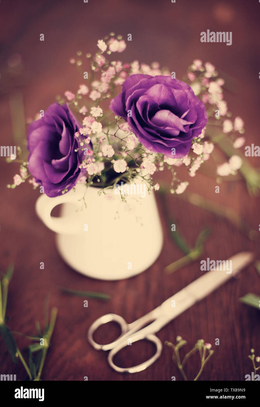 fresh cut purple flowers in a vase on a wooden table with scissors Stock Photo
