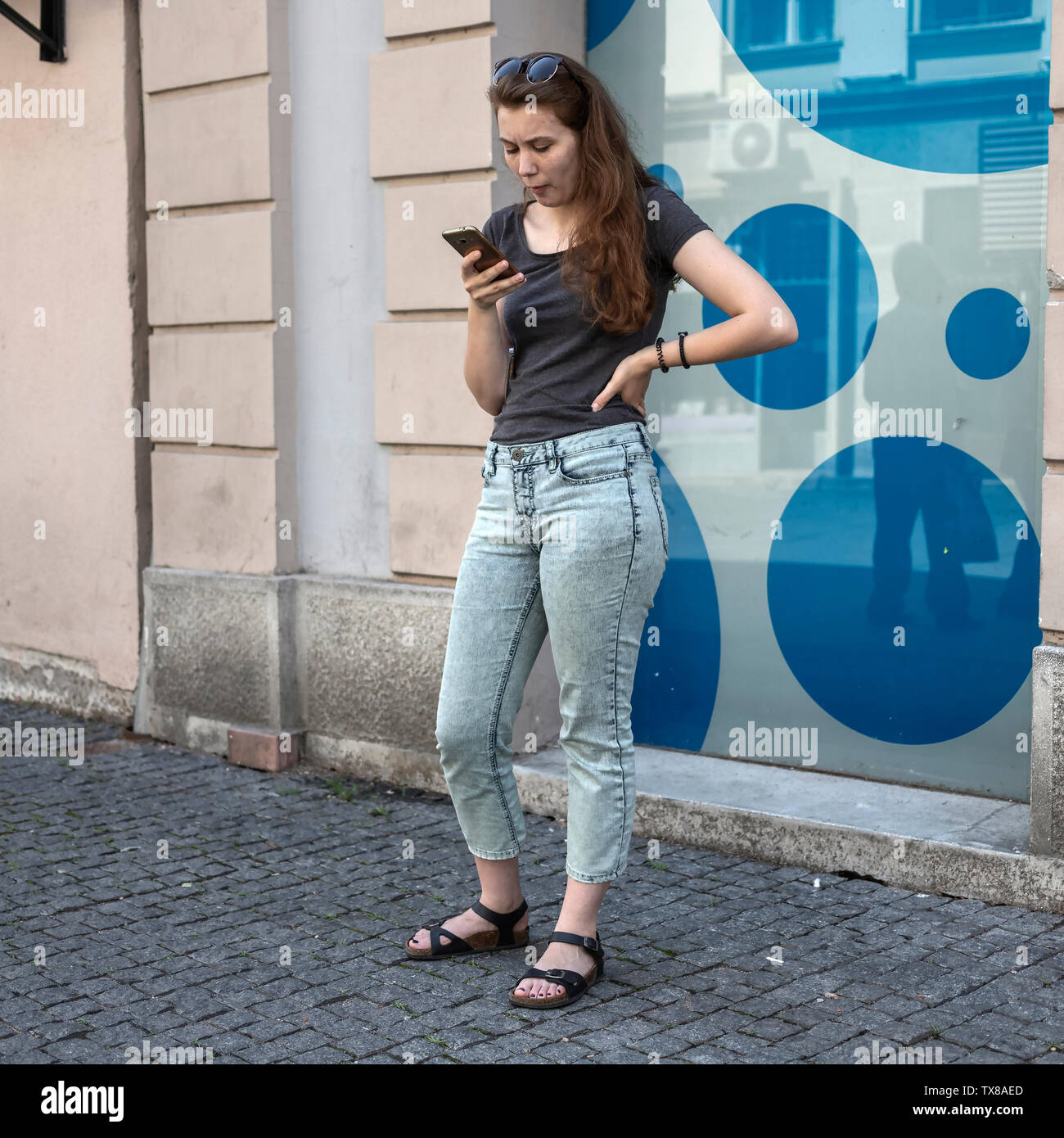 Belgrade, Serbia, June 22nd 2019: Urban scene with young woman standing on the street and handling her mobile phone Stock Photo