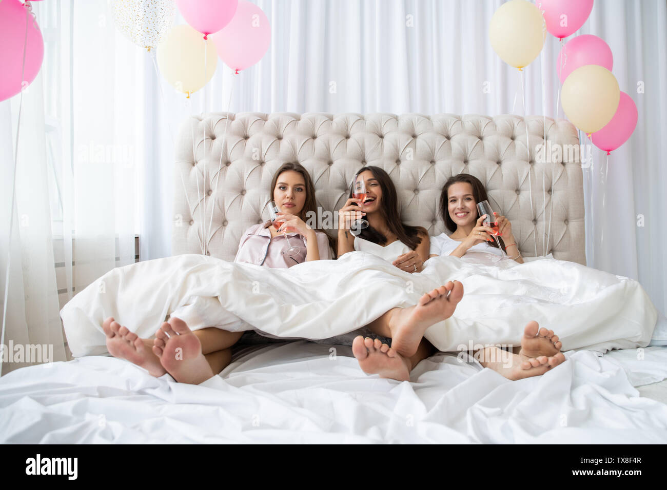 Pajama party. Attractive young smiling women in pajamas drinking champagne  while having a slumber party in the bedroom Stock Photo - Alamy