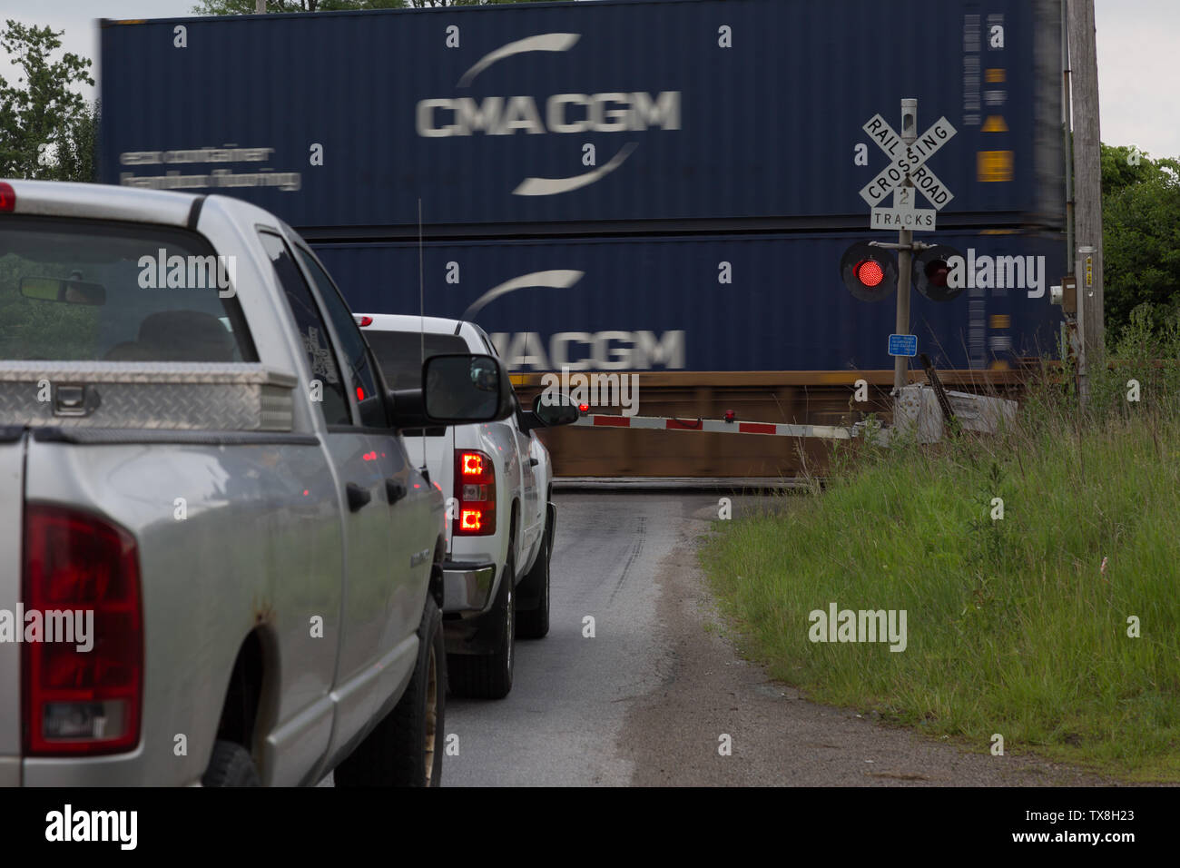 Two pickup trucks wait in line at a DeKalb County, Indiana, CSX railroad crossing as a train passes. Stock Photo