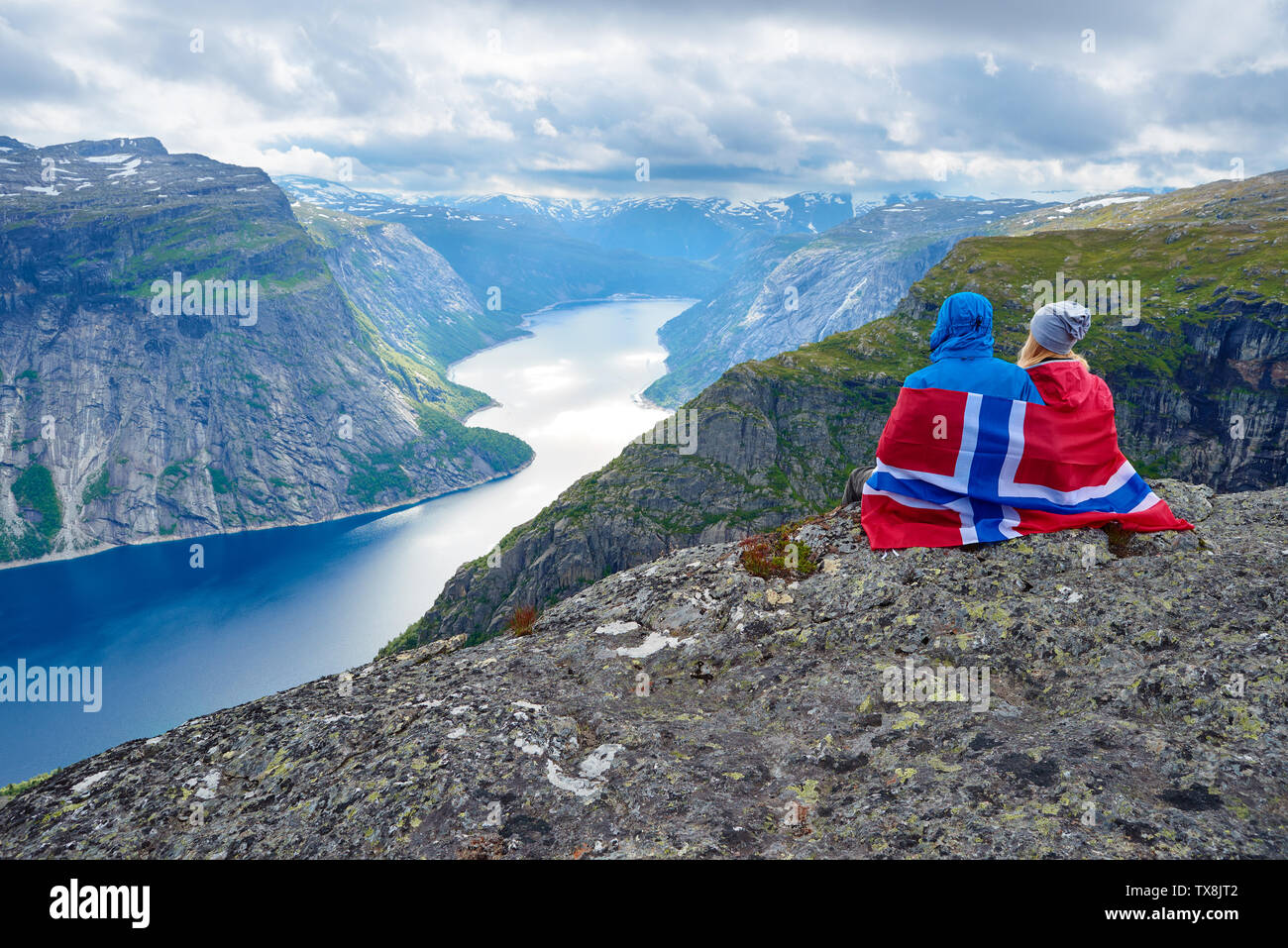 Couple sits on rock and looks at mountains near Trolltunga. Popular tourist attraction. Ringedalsvatnet - lake in the municipality of Odda in Hordalan Stock Photo