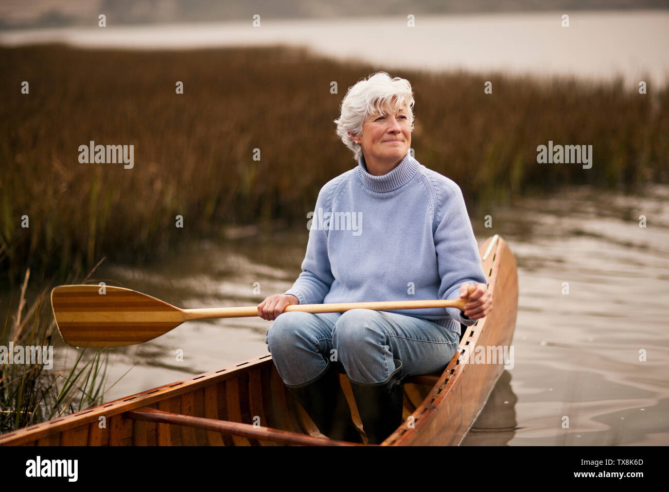 Mature woman smiles and looks away as she holds an oar ready to row and ...