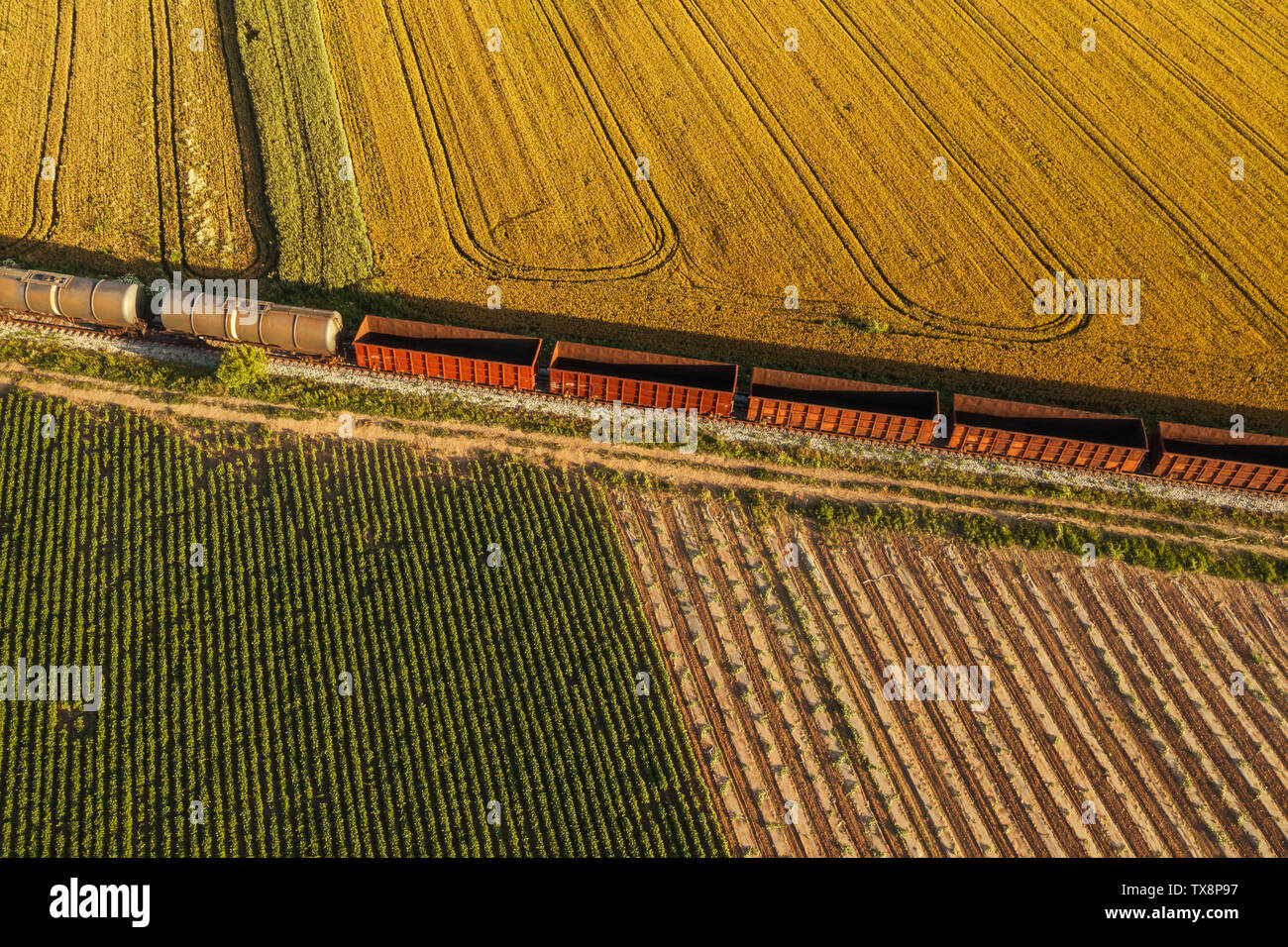 Rail freight transport, aerial view of train passing on railway through cultivated fields in countryside Stock Photo