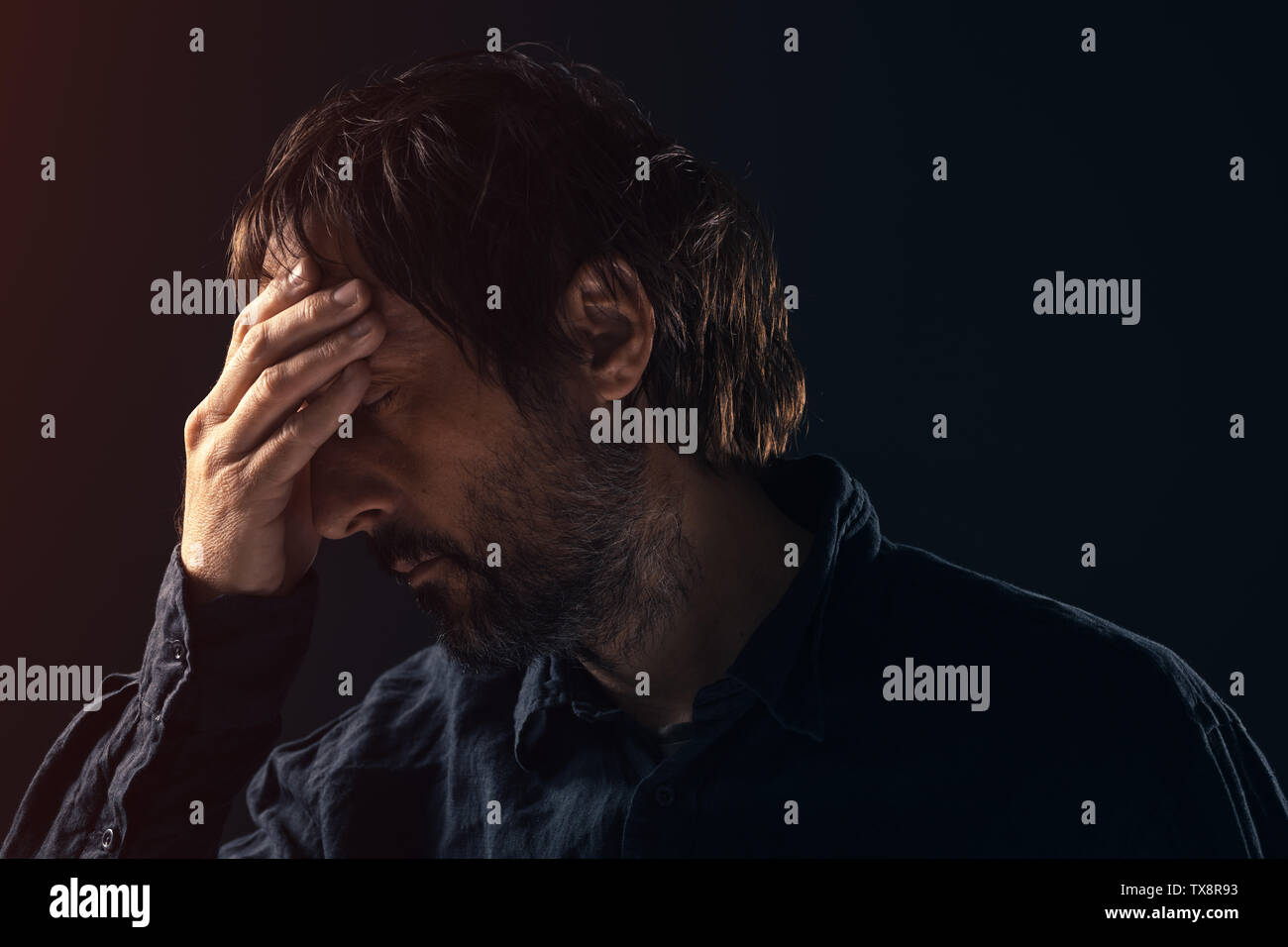 Depressed sad mid-adult man. Low key portrait of male person feeling heartbroken. Distraught state of mind and mental health concept. Stock Photo