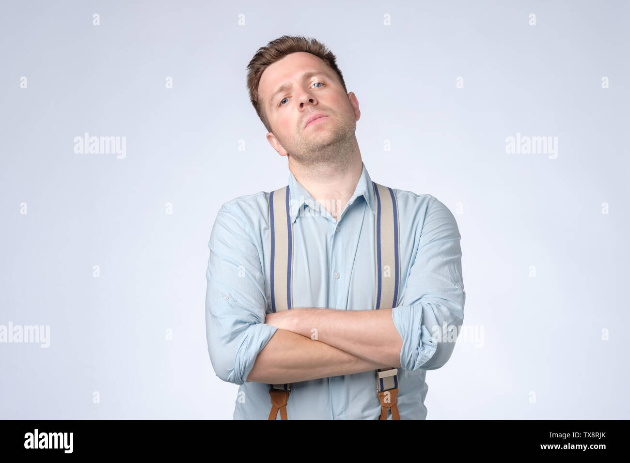 Serious selfish man with folded arms and suspenders posing at studio. Stock Photo