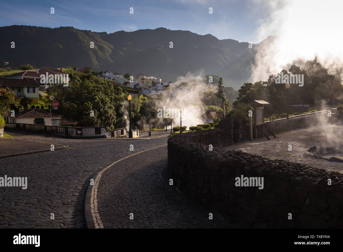 Sunny morning in a small city in a valley, with many natural hot springs, creating a steam, highlighted by the sunshine. Typical paved road and paveme Stock Photo