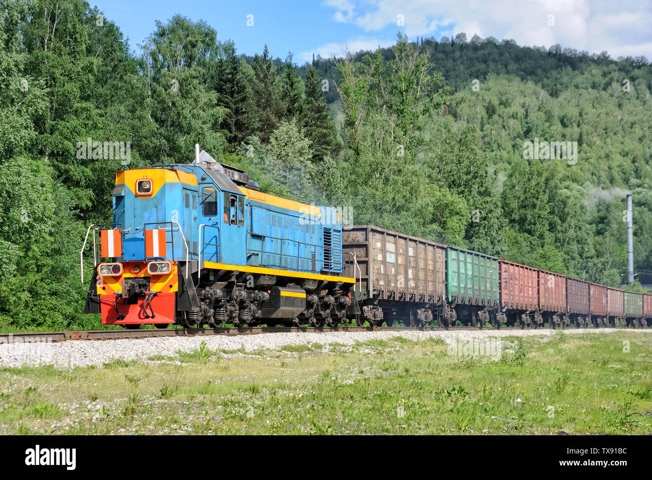 = Diesel Locomotive with Freight Train in Mezhdurechensk =  Colorful diesel locomotive with empty freight train running through the mountains to load Stock Photo