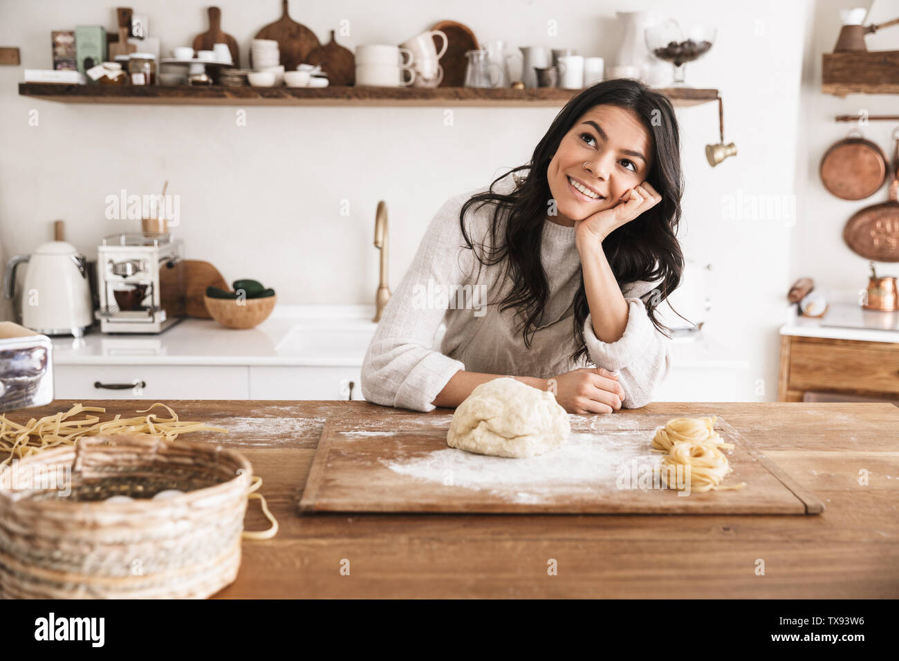 Portrait of smiling european woman 30s wearing apron cooking and making homemade pasta of dough in kitchen at home Stock Photo