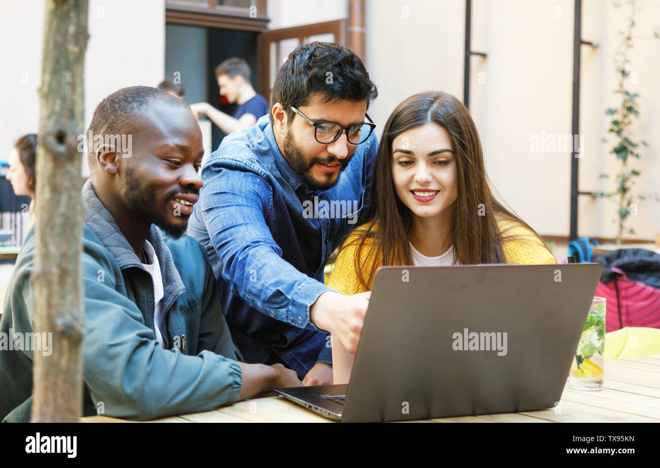 Three multicultural students discussing something at the laptop while studying at the cafe Stock Photo