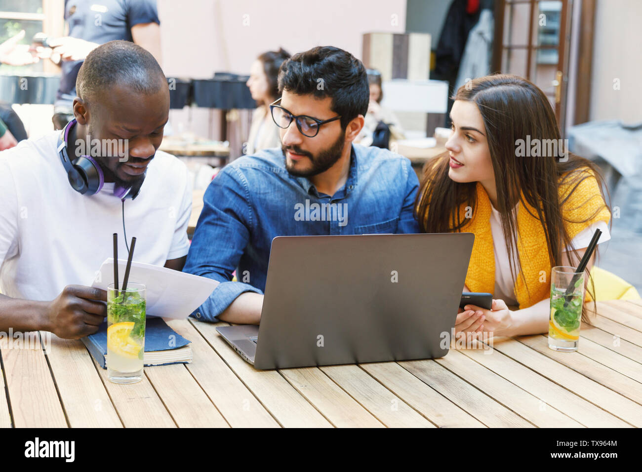 Three multicultural smart students preparing homework tasks at the outdoor cafe Stock Photo