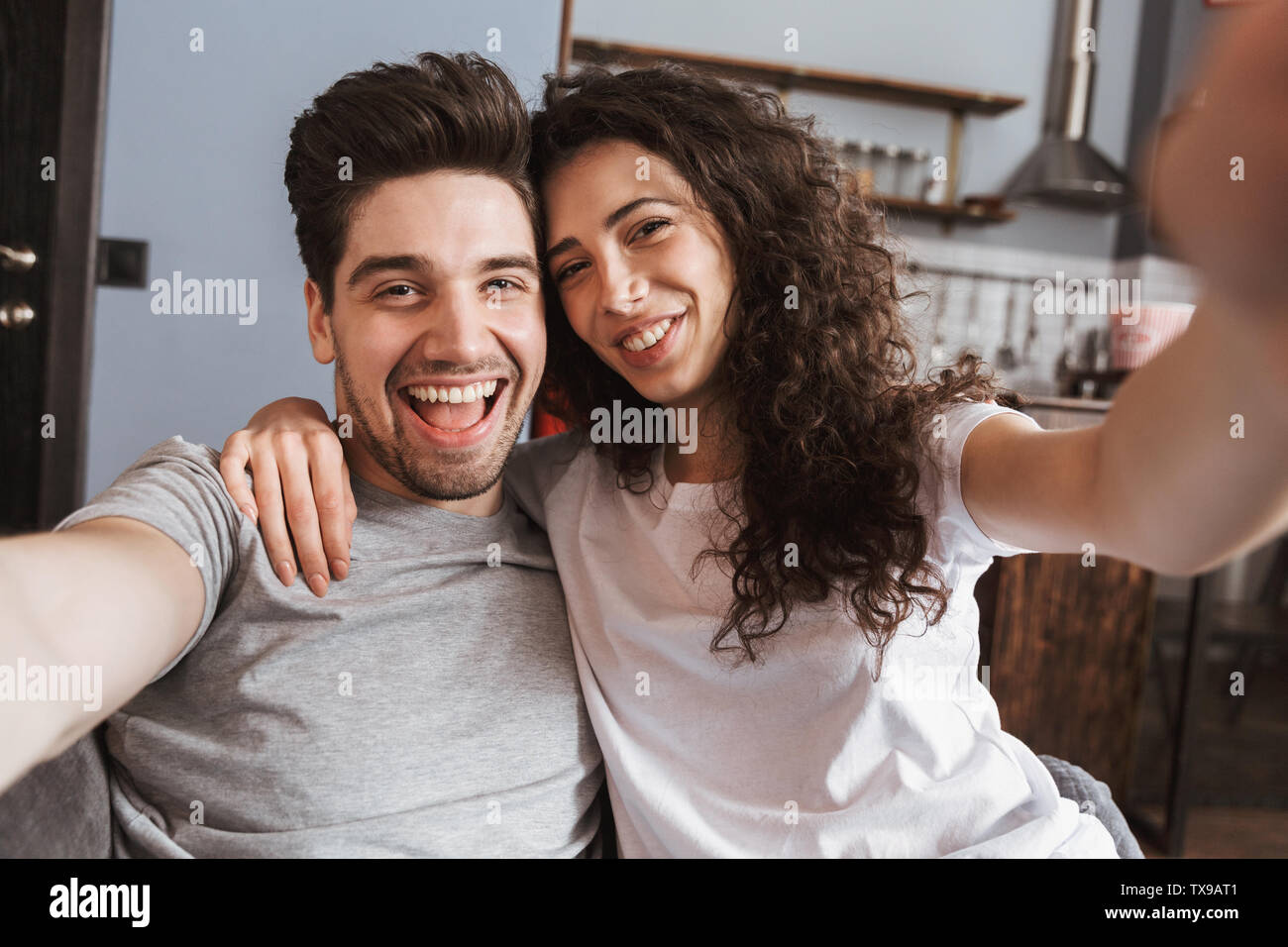 Cheerful young couple relaxing on a couch at home, taking a selfie ...