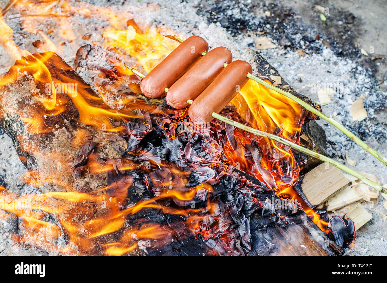 Grilling sausages over an open fire outdoors Stock Photo