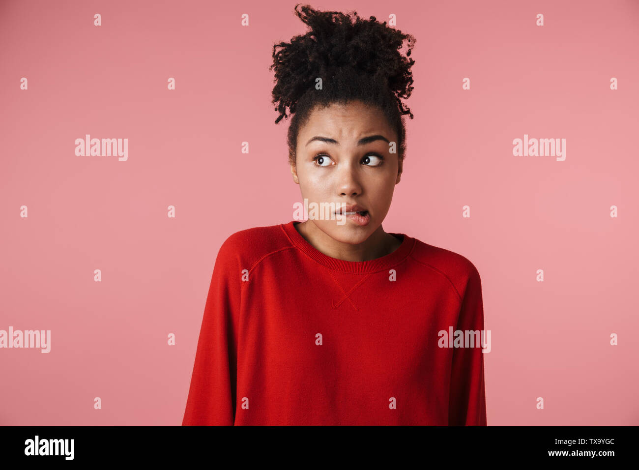 Image closeup of embarrassed african american woman looking aside and biting her lip isolated over pink background Stock Photo
