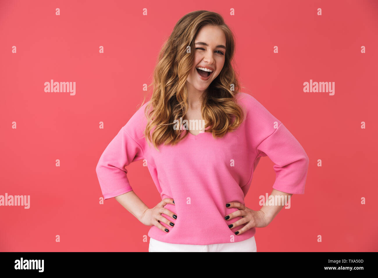 Beautiful young casual blonde girl standing isolated over pink background, hands on hips Stock Photo