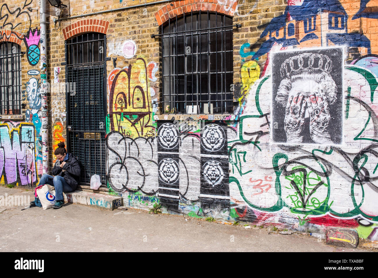 Woman sitting in front of graffiti in the famous Shoreditch Graffiti Wall at Seven Stars Yard, a yard filled with street art near Brick Lane Stock Photo
